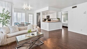 A modern living room with a sofa, coffee table, and a view into the kitchen. - Modern Cozy Retreat With Pool Fireplace (Pomona)