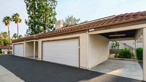 A residential garage with three white garage doors, a tiled roof, and a concrete driveway. - Modern Cozy Retreat With Pool Fireplace (Pomona)