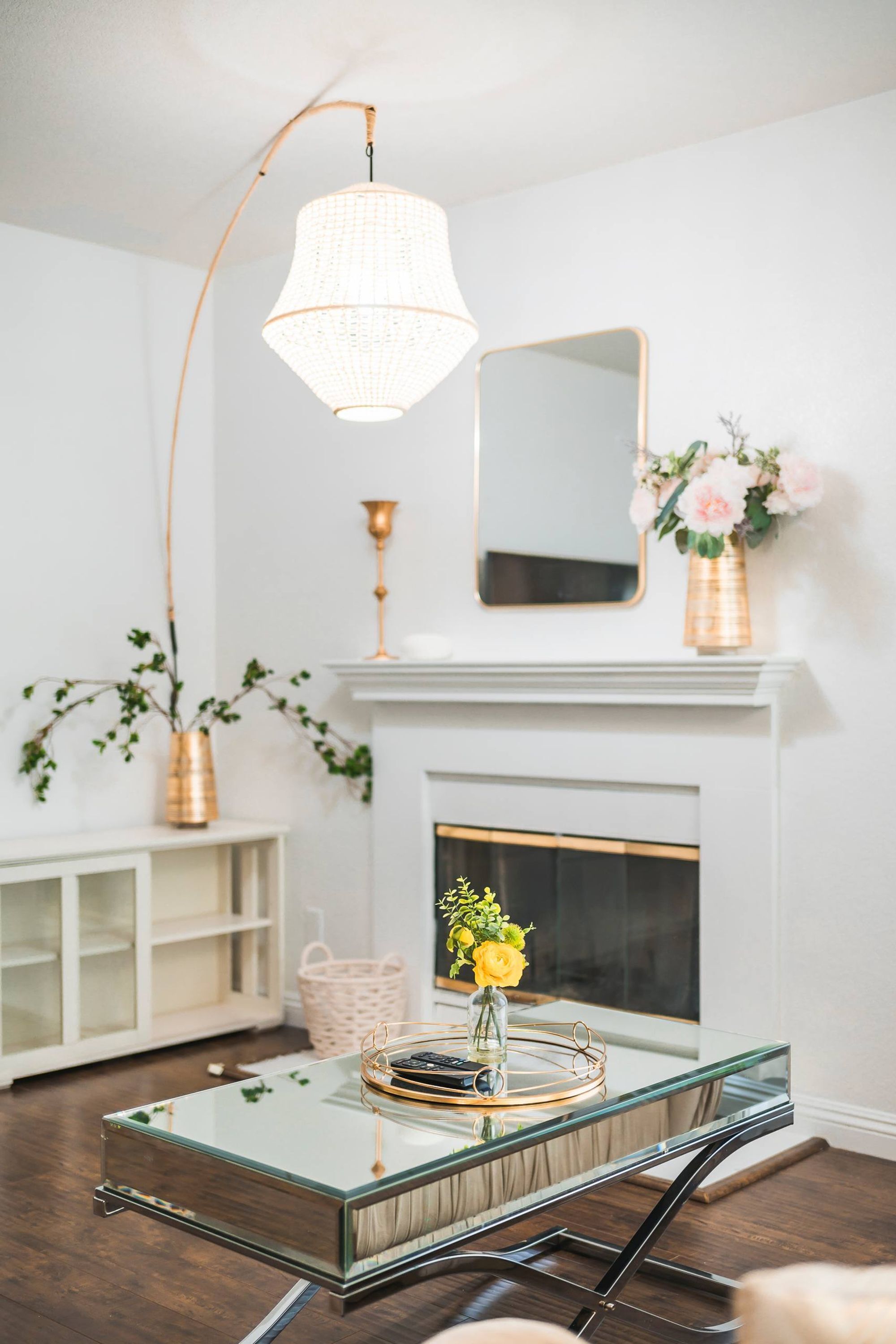 Un salon moderne avec une table basse en verre, une cheminée blanche et un luminaire suspendu.