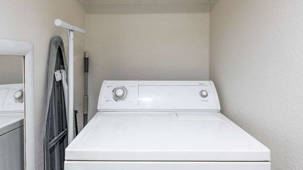 A laundry room with a front-loading washer and dryer, a drying rack, and a utility shelf above the dryer. - Modern Cozy Retreat With Pool Fireplace (Pomona)