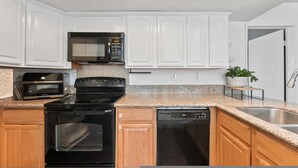 A kitchen with white cabinets, a microwave, a stove, and a dishwasher. - Modern Cozy Retreat With Pool Fireplace (Pomona)
