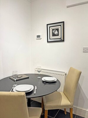 A dining area with a round table, two chairs, a framed picture on the wall, a thermostat, and a radiator.