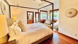A spacious four-poster bed with a wooden ceiling fan, a large window offering a view of the outdoors, and a small round table with a chair. - Short Walk to Beach Hanalei Bay (Hanalei)