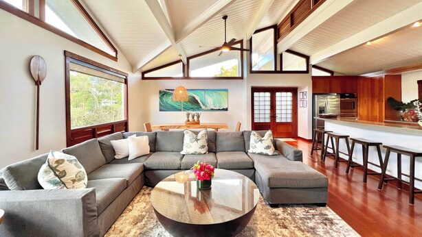 A modern living room with a sectional sofa, a round coffee table, and a dining area with bar stools. - Short Walk to Beach Hanalei Bay (Hanalei)