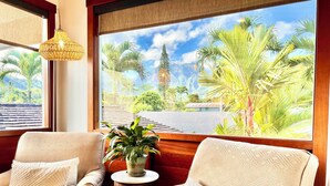 A room with two beige armchairs, a small round table with a plant, and a view of tropical scenery through large windows. - Short Walk to Beach Hanalei Bay (Hanalei)