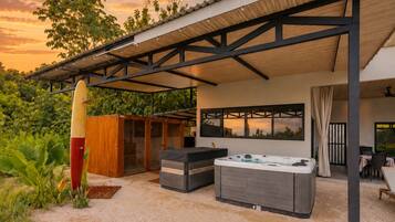 Un patio exterior con un jacuzzi, mobiliario y una zona cubierta con vistas al atardecer.