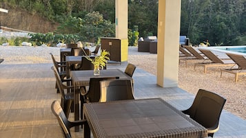 Een terras buiten met tafels en stoelen, een zwembad en uitzicht op het omliggende bos.