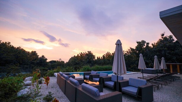 A poolside area with lounge chairs and umbrellas, surrounded by natural vegetation and a clear sky.