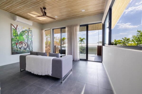 A modern bedroom with a bed, a ceiling fan, a large window, and a painting.