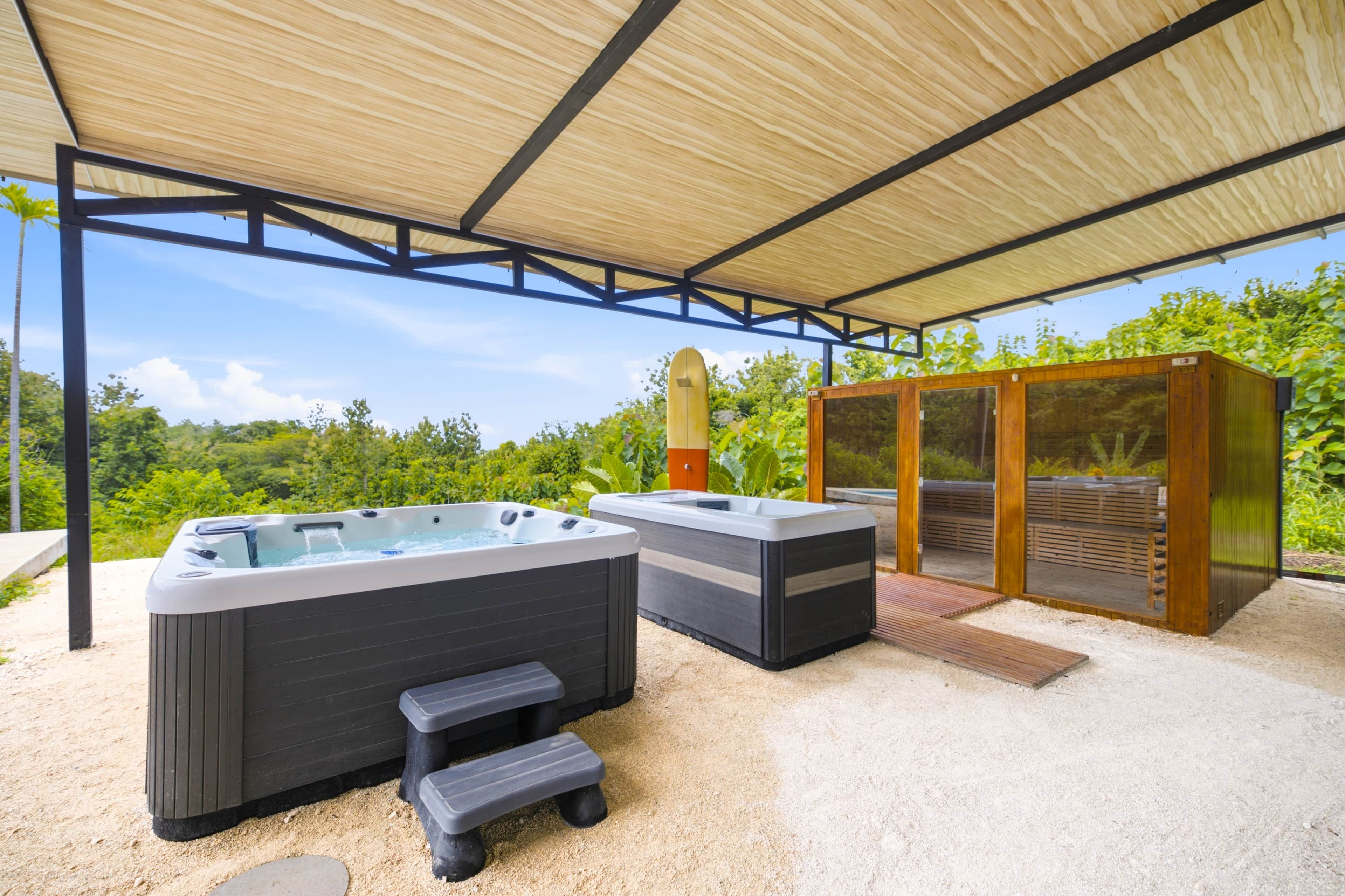 Een overdekt buitengebied met twee whirlpools, een houten bank en een houten constructie met glazen deuren.