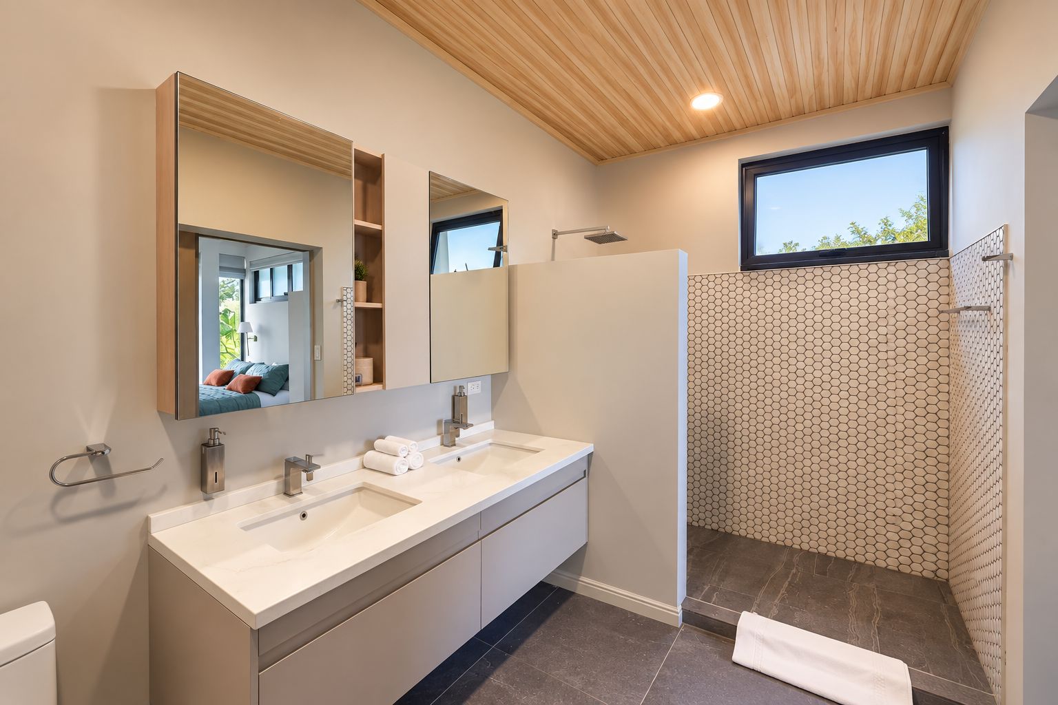 Un baño moderno con tocador de doble lavabo, un espejo grande, cabina de ducha y ventana que proporciona luz natural.