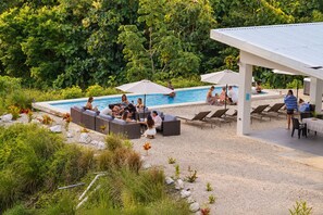Un área junto a la piscina con sillones de descanso y una zona de estar cubierta.