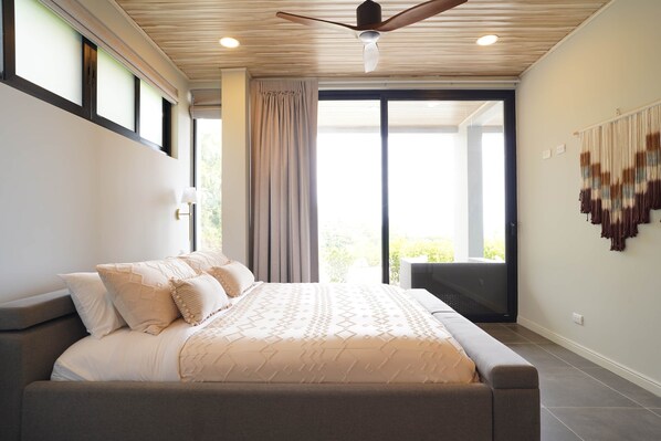 Een moderne slaapkamer met een groot bed, een plafondventilator en uitzicht op de omgeving.
