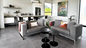 Una sala de estar moderna con un sofá seccional gris, una mesa de centro y un comedor con una cocina al fondo.