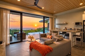 Een moderne woonkamer met een bank, een bijzettafeltje en uitzicht op de ondergaande zon.
