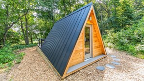A small, triangular wooden cabin with a dark roof, surrounded by a forest. - New A-Frame Tiny Home Retreat -With Private Sauna! (Christiana)