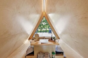 Une tente triangulaire en bois, confortable, avec une table, une chaise et une vue sur la verdure environnante.