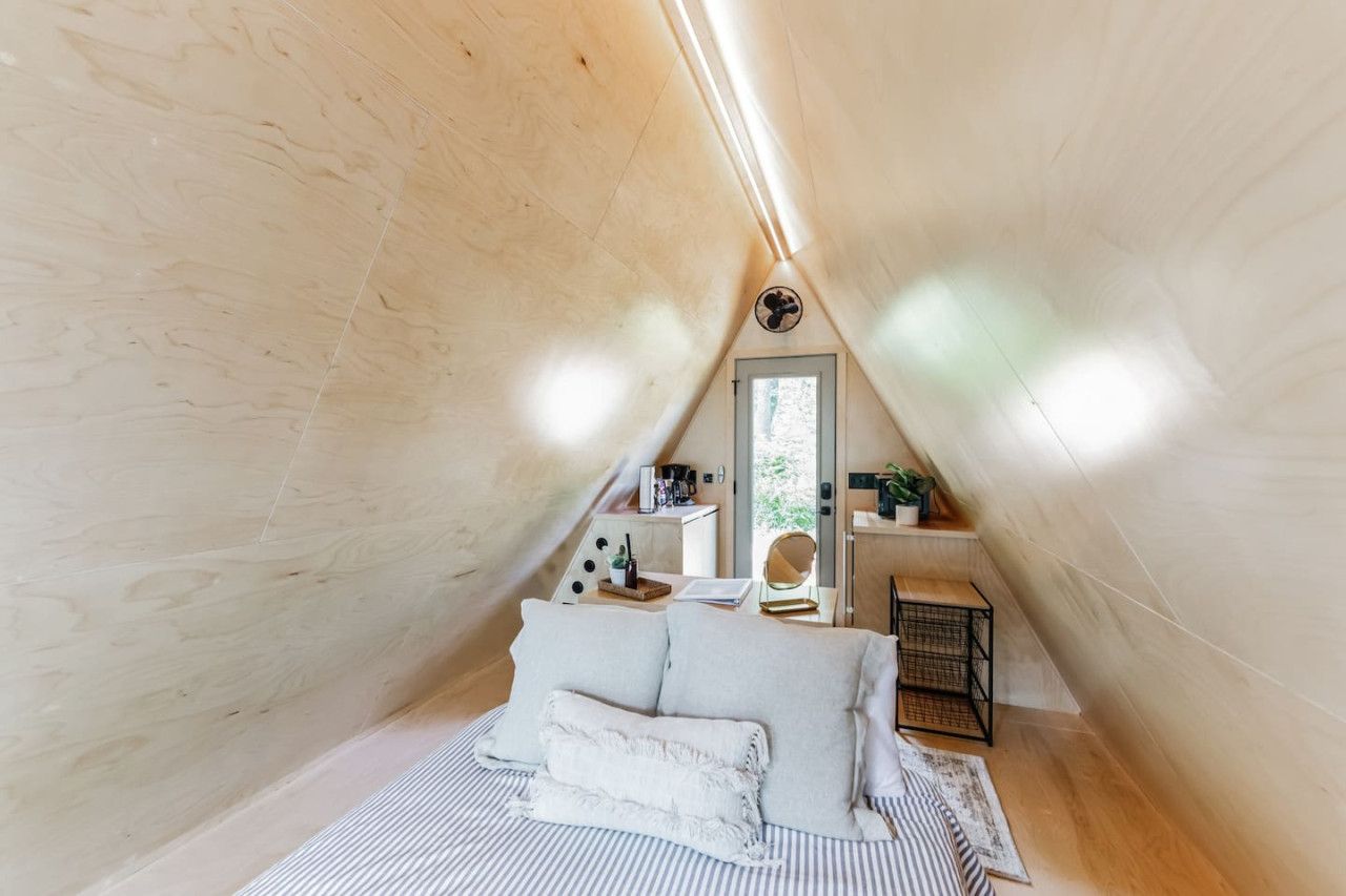 A cozy attic bedroom with a sloped ceiling, a bed with white linens, a small desk with a chair, and a window providing natural light.