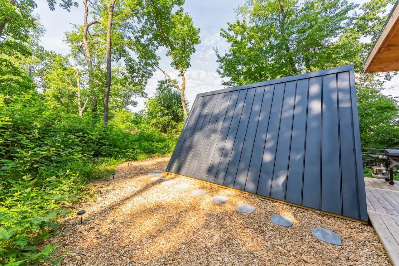 A modern outdoor deck with a sloped roof, surrounded by dense greenery and trees.