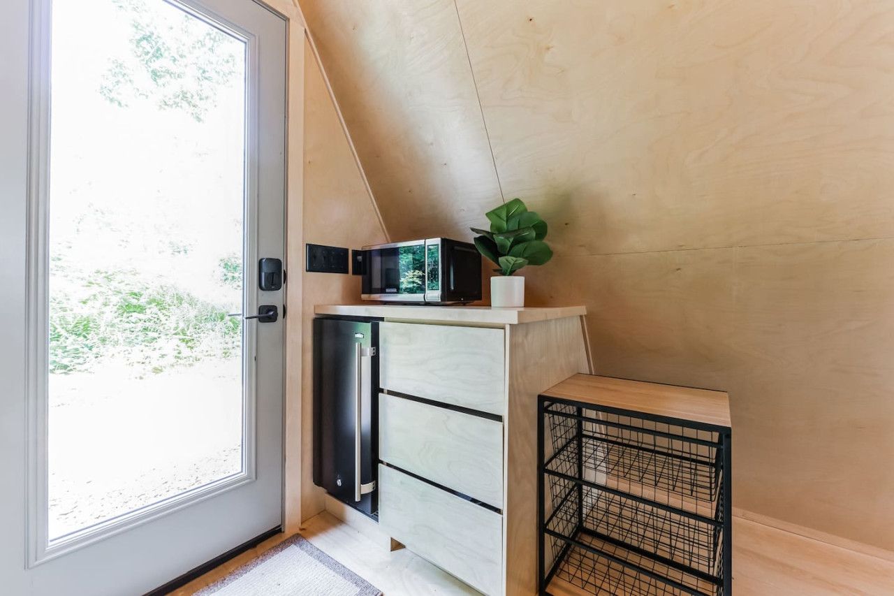 A compact kitchen with a built-in microwave, a small refrigerator, and a potted plant on a wooden shelf.