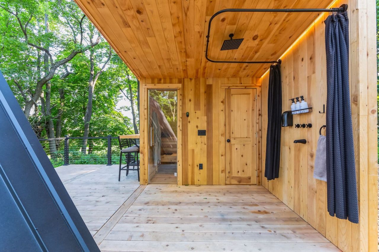 A wooden cabin with a wooden floor, a door, and a small table with chairs outside.