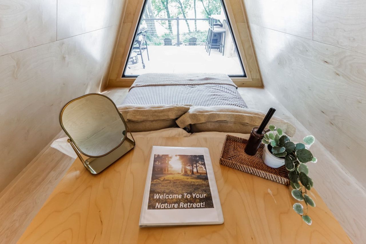 Una habitación acogedora con una cama, un espejo, un cartel de bienvenida y una planta pequeña.