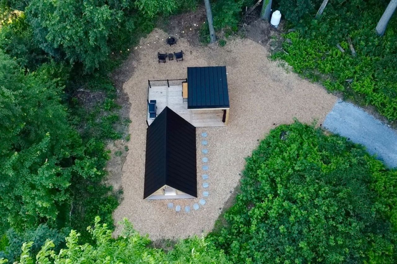 An aerial view of a small, enclosed outdoor area with a black-roofed structure, a seating area with chairs and a table, and a paved path.
