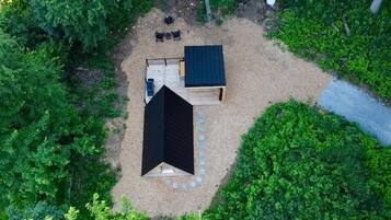 An aerial view of a small, enclosed outdoor area with a black-roofed structure, a seating area with chairs and a table, and a paved path.
