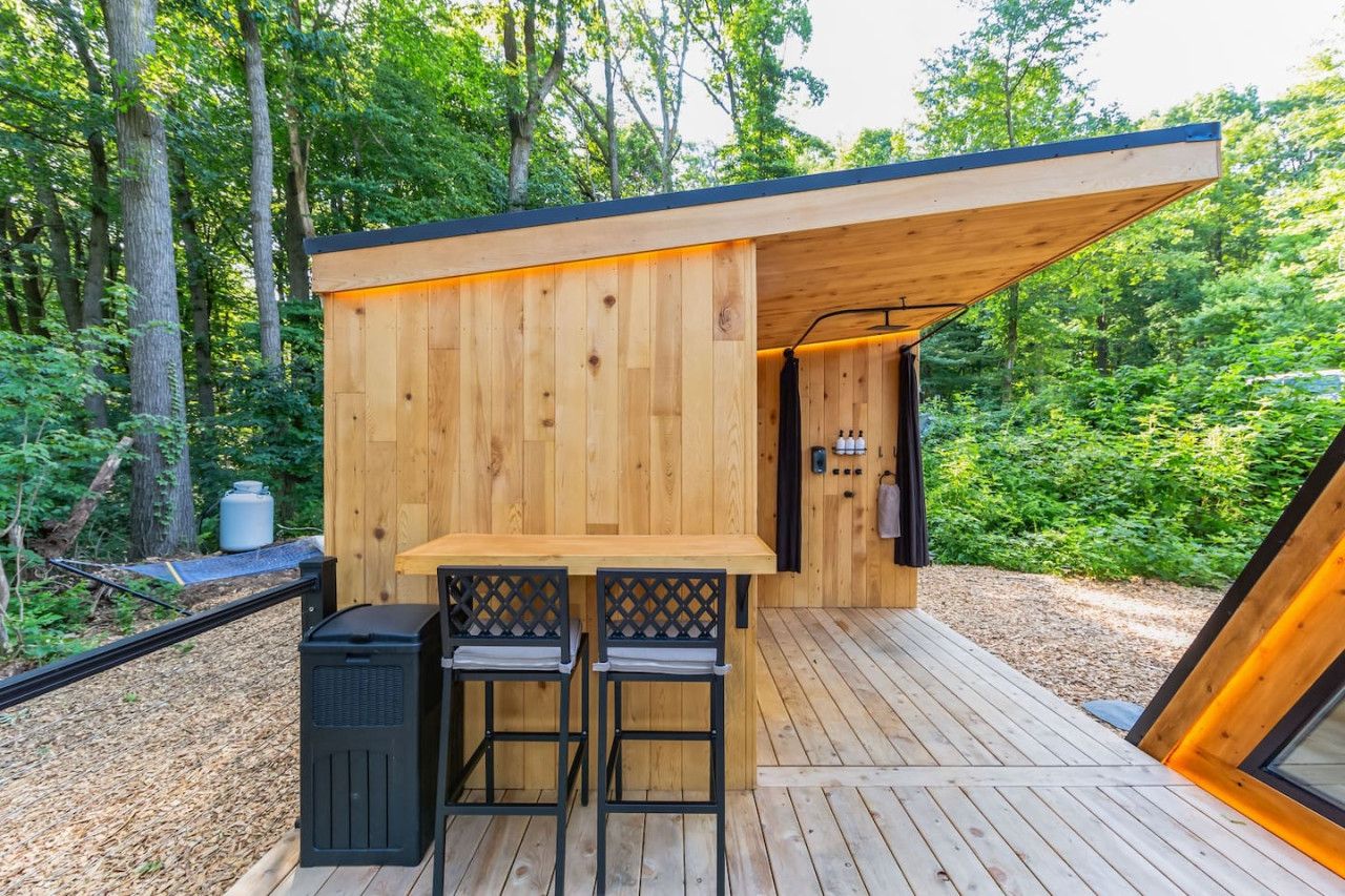 A wooden cabin with a deck, two chairs, a table, and a small kitchen area.