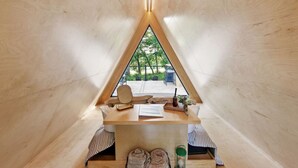 A cozy, triangular wooden tent with a table, a chair, and a view of greenery outside. - New A-Frame Tiny Home Retreat -With Private Sauna! (Christiana)
