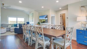 Un coin repas avec une table en bois et des chaises en osier, un buffet bleu et une vue sur l’extérieur par une fenêtre.