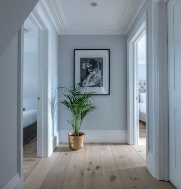 En hall med ett inramat svartvitt fotografi på väggen, en krukväxt och trägolv.