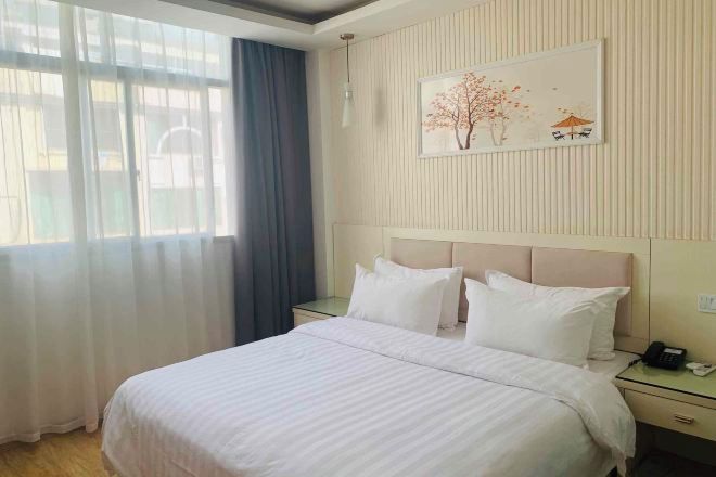 Una habitación de hotel con una cama, mesitas de noche, un teléfono y una ventana con cortinas.