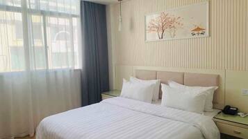 Una habitación de hotel con una cama, mesitas de noche, un teléfono y una ventana con cortinas.