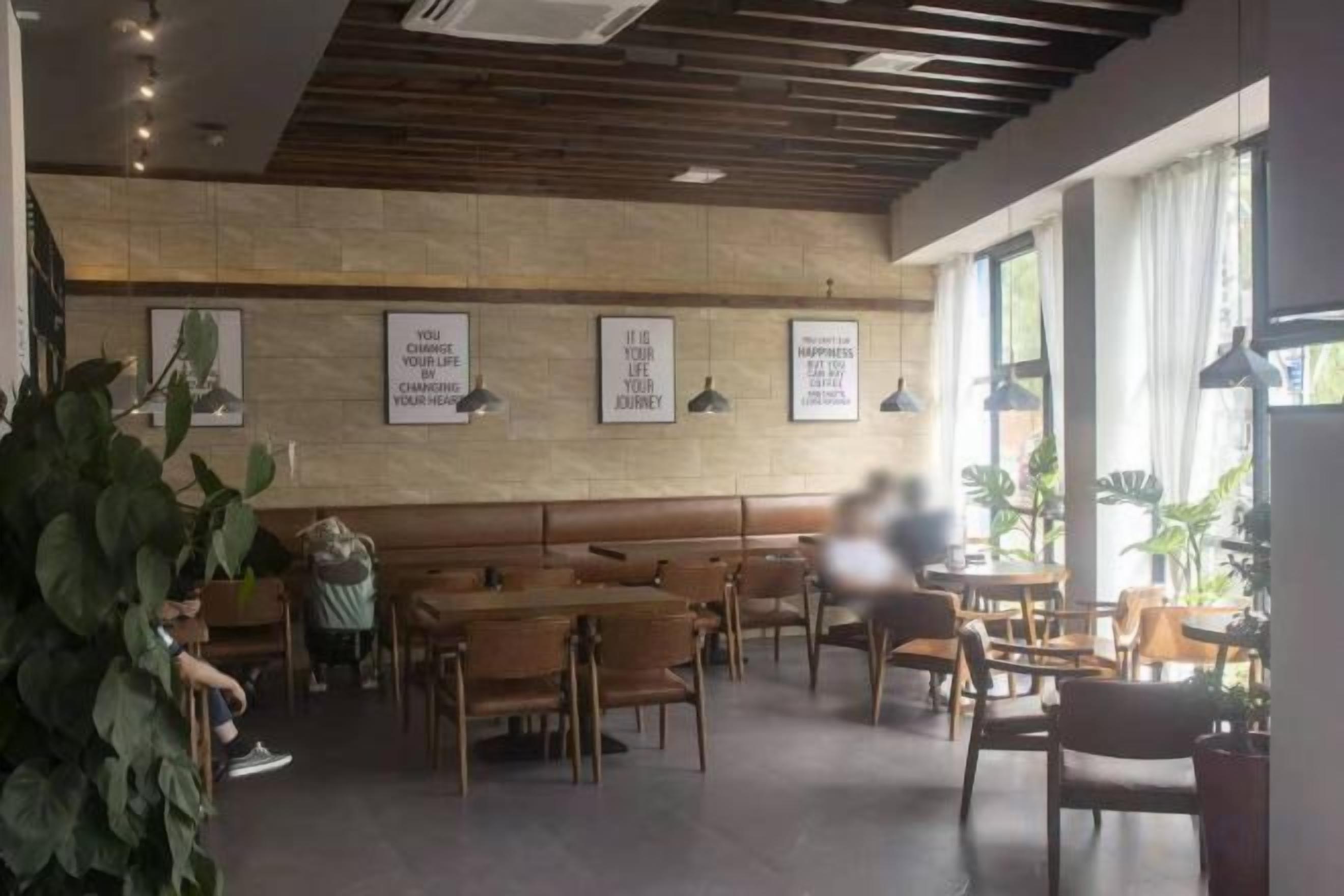 A cafe interior with wooden tables and chairs, framed inspirational quotes on the wall, and potted plants.