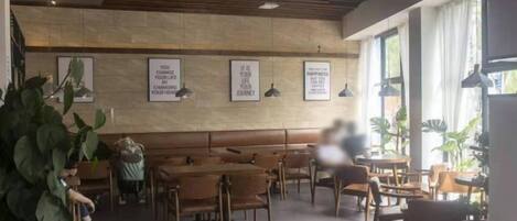 Ein Café-Interieur mit Holztischen und -stühlen, gerahmten Motivationssprüchen an der Wand und Zimmerpflanzen.