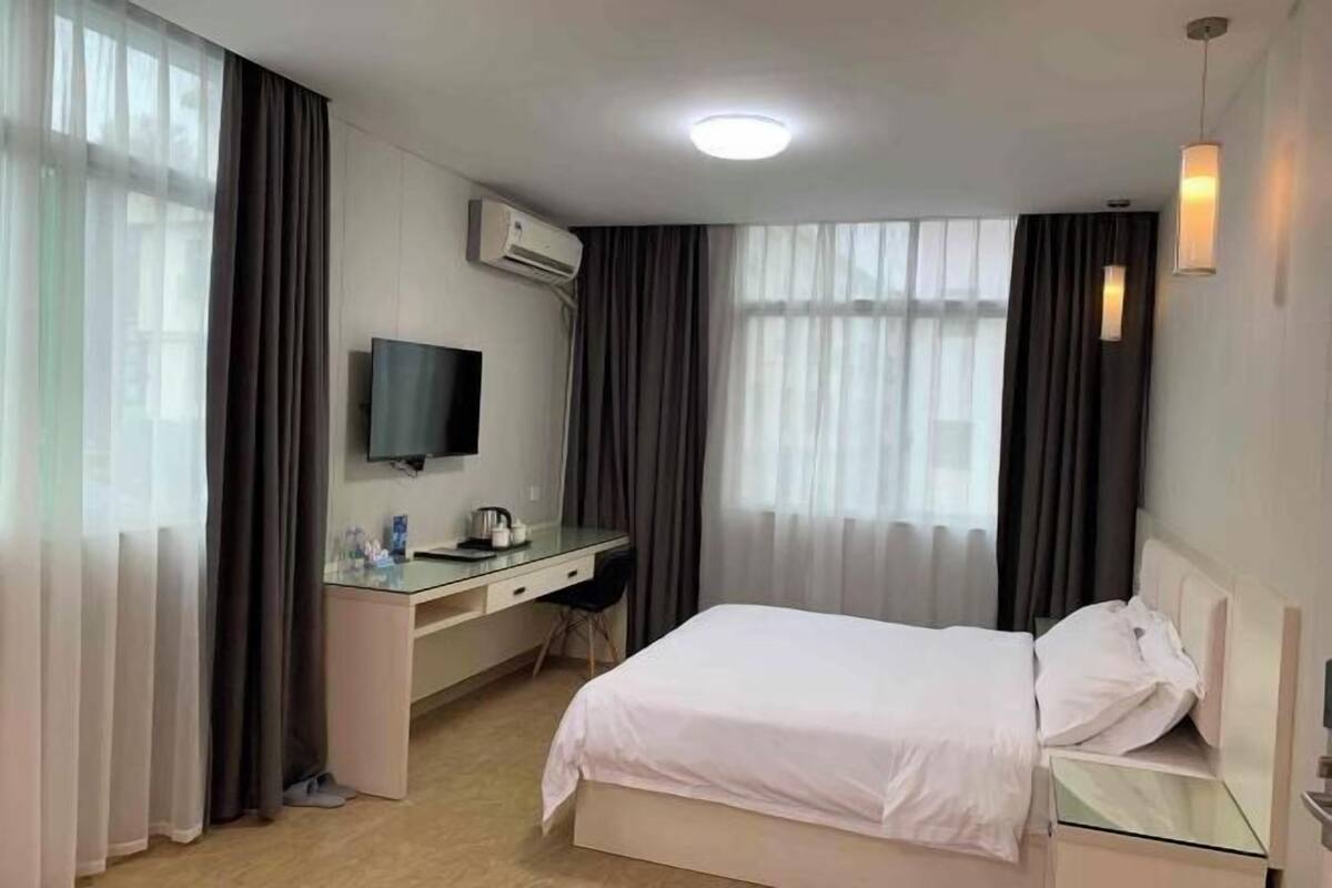 Ein Hotelzimmer mit Bett, Schreibtisch, Stuhl, Fernseher und einem Fenster mit Vorhängen.