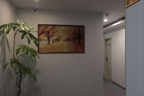 A corridor with a framed painting on the wall, a potted plant, and a door at the end.