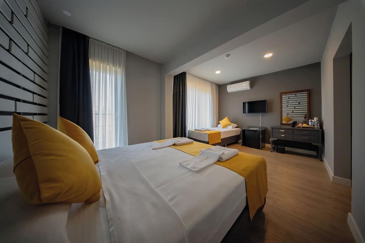 Quarto de hotel com uma cama grande, escrivaninha, televisão e janela com cortinas.