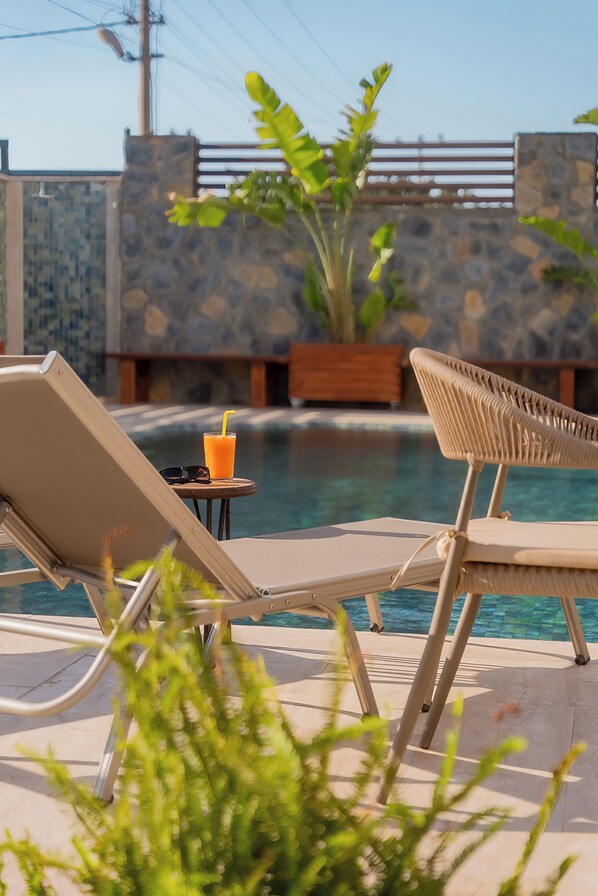 A poolside area with lounge chairs, a drink, and a stone wall in the background. - Neko Hotel (Bodrum)
