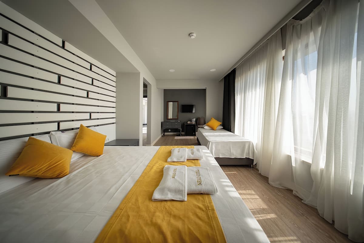 Quarto de hotel moderno com uma cama grande, duas camas menores, uma escrivaninha e uma televisão.