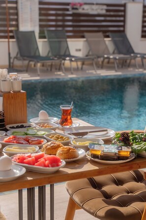 A breakfast table with various dishes and a glass of tea by a poolside.