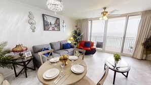 Ein Wohnzimmer mit Esstisch für vier Personen, einer Couch, einem roten Sessel und einem Balkon mit Aussicht.