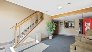 A staircase with wooden railings, a potted plant, a trash bin, and a Coca-Cola refrigerator in a room with carpeted flooring and a couch. - Pelican Lakes Motel (Pequot Lakes)
