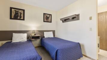 Habitación de hotel con dos camas, una mesita de noche con lámpara y dos cuadros en la pared.