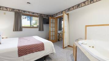 A hotel room with two beds, a bathroom with a bathtub, and a view of the outside.