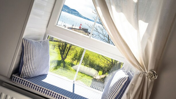 A window seat with striped cushions, a view of a lake, and a red structure in the distance.
