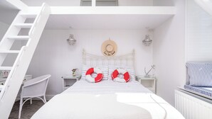 A bedroom with a bed, a white chair, a nightstand, a dresser, a hat on the wall, and a ladder.