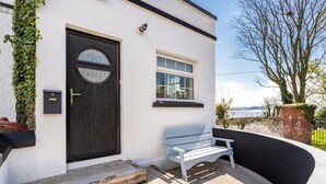 A white building with a black door, a window, and a bench outside.