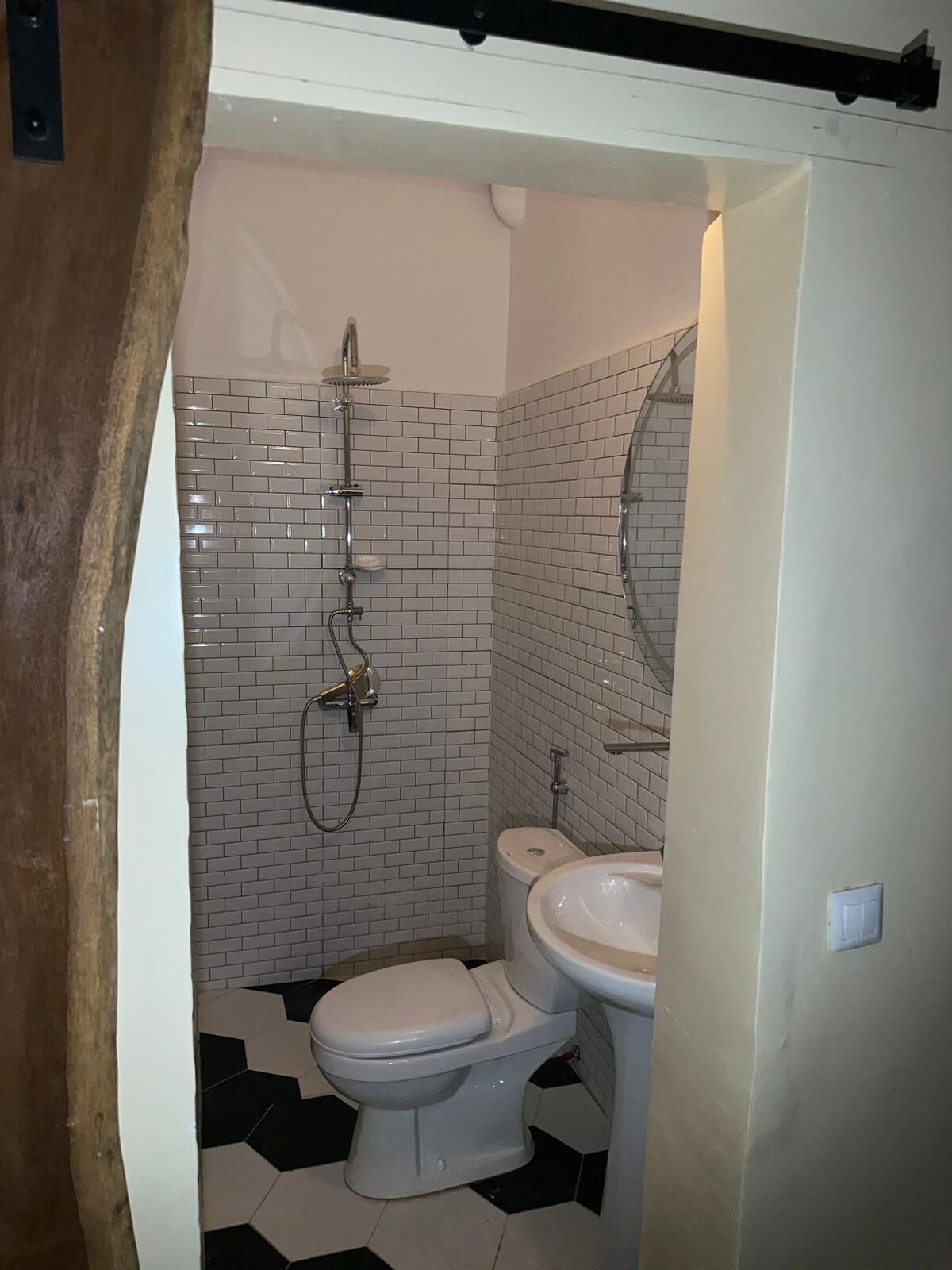 A bathroom with a shower, toilet, and sink, featuring white subway tiles and a black and white tiled floor.